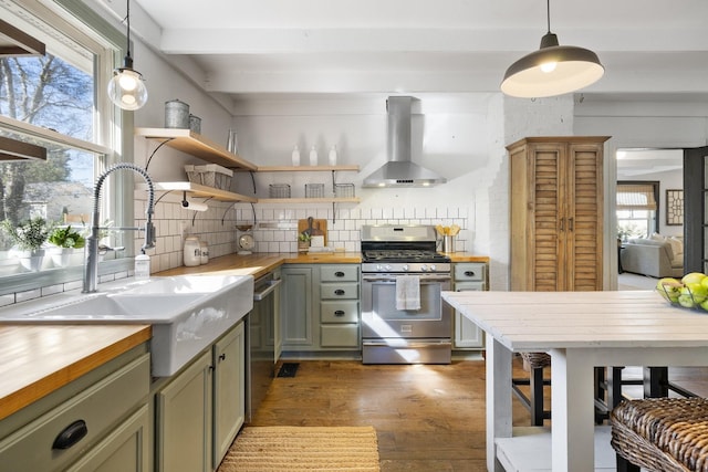 kitchen with appliances with stainless steel finishes, pendant lighting, wooden counters, and wall chimney exhaust hood