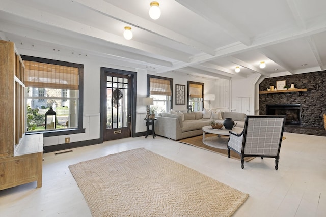 living room featuring a stone fireplace, a healthy amount of sunlight, and beam ceiling