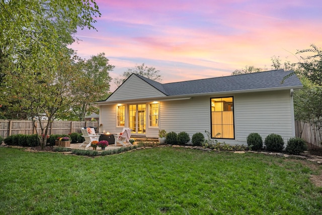 back house at dusk featuring a patio area and a lawn