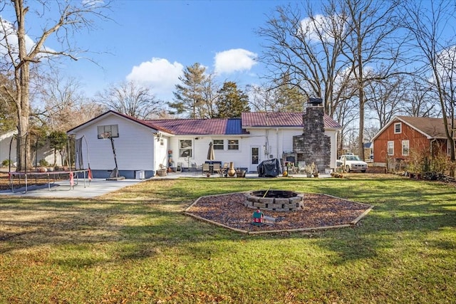 rear view of property with a patio, a fire pit, a trampoline, and a lawn