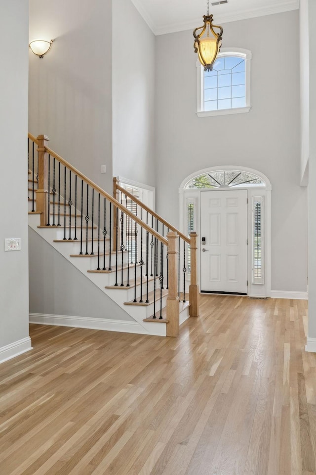 foyer entrance with crown molding, a high ceiling, and light wood-type flooring