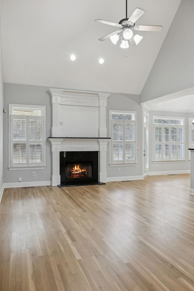 unfurnished living room featuring ceiling fan, a healthy amount of sunlight, a high end fireplace, and light hardwood / wood-style floors