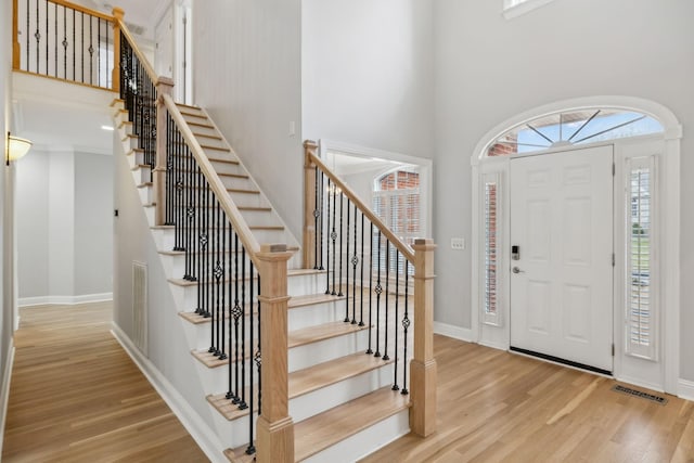 foyer with a towering ceiling, a wealth of natural light, and light wood-type flooring