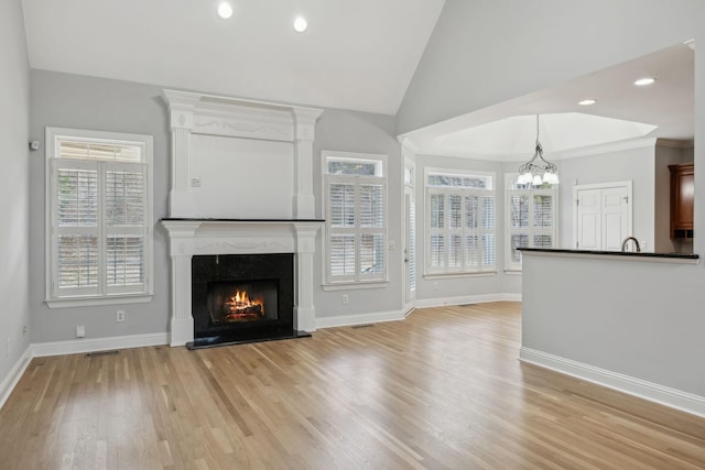 unfurnished living room featuring a premium fireplace, high vaulted ceiling, a notable chandelier, and light hardwood / wood-style floors