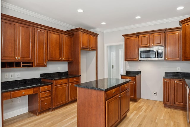 kitchen with built in desk, dark stone counters, ornamental molding, a center island, and light hardwood / wood-style floors