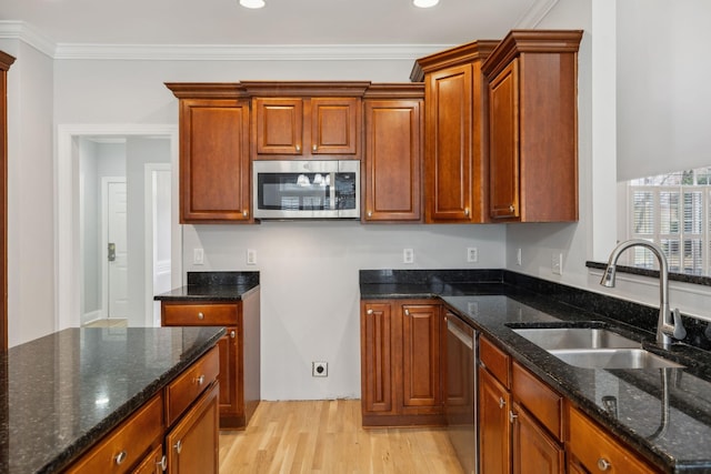 kitchen featuring sink, dark stone countertops, stainless steel appliances, crown molding, and light hardwood / wood-style flooring