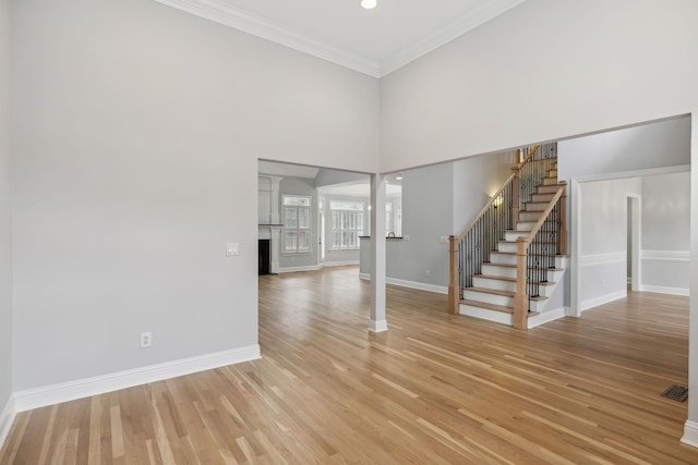 unfurnished living room featuring a high ceiling, ornamental molding, and light wood-type flooring