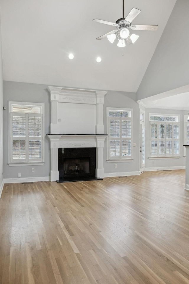 unfurnished living room featuring ceiling fan, high vaulted ceiling, a high end fireplace, and light hardwood / wood-style floors