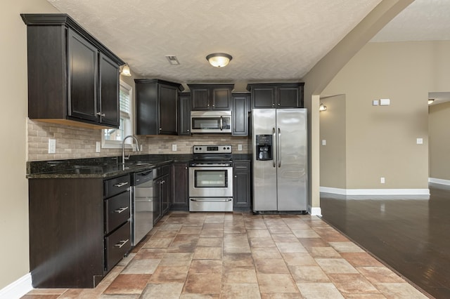 kitchen with appliances with stainless steel finishes, sink, backsplash, dark stone counters, and a textured ceiling