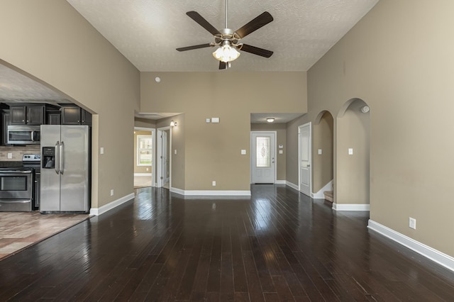 unfurnished living room featuring dark wood-type flooring, ceiling fan, a textured ceiling, and a high ceiling