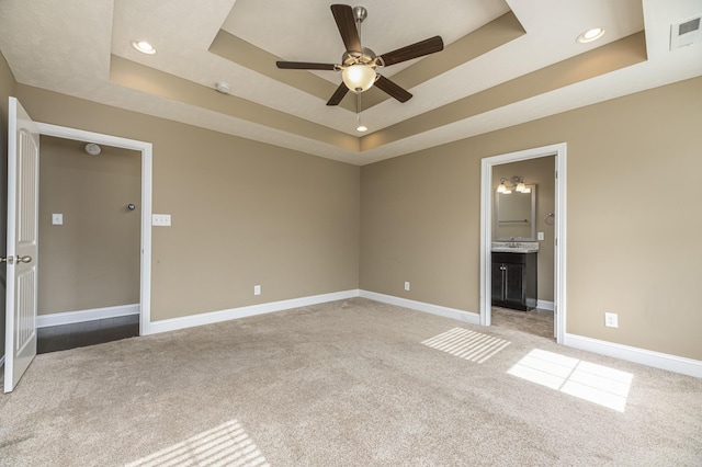 unfurnished bedroom with a raised ceiling, carpet floors, connected bathroom, and ceiling fan