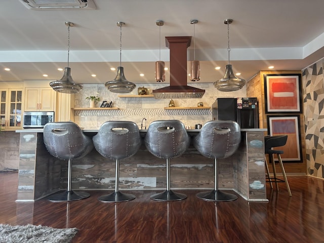 kitchen featuring stainless steel microwave, wood finished floors, freestanding refrigerator, a breakfast bar area, and island range hood