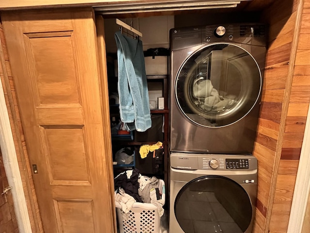 clothes washing area with laundry area, wood walls, and stacked washer and clothes dryer