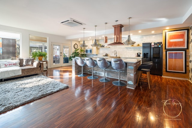 kitchen with backsplash, a kitchen bar, island exhaust hood, black fridge with ice dispenser, and dark wood-style flooring