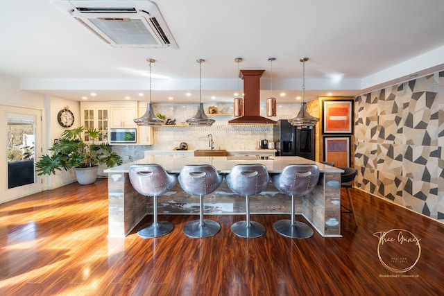 kitchen featuring a breakfast bar area, island exhaust hood, a large island, glass insert cabinets, and stainless steel microwave