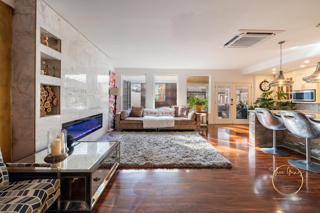 living area with a tile fireplace, a wall mounted AC, french doors, and wood finished floors