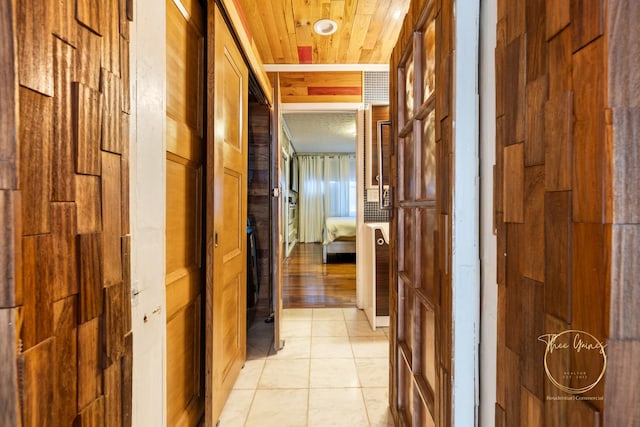 hallway featuring light tile patterned floors, wooden walls, and wood ceiling