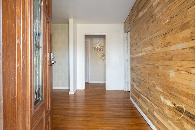 corridor with dark wood finished floors, wooden walls, and baseboards