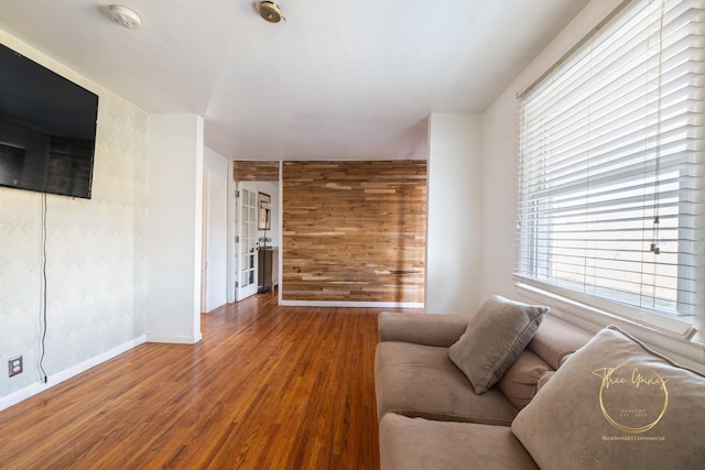 living room with baseboards, wooden walls, and wood finished floors