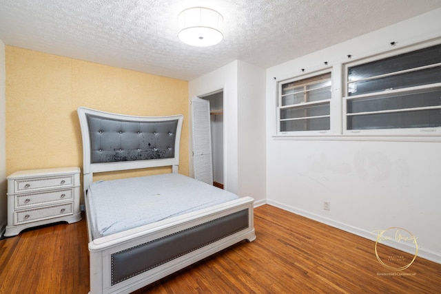 unfurnished bedroom with a closet, a textured ceiling, baseboards, and wood finished floors