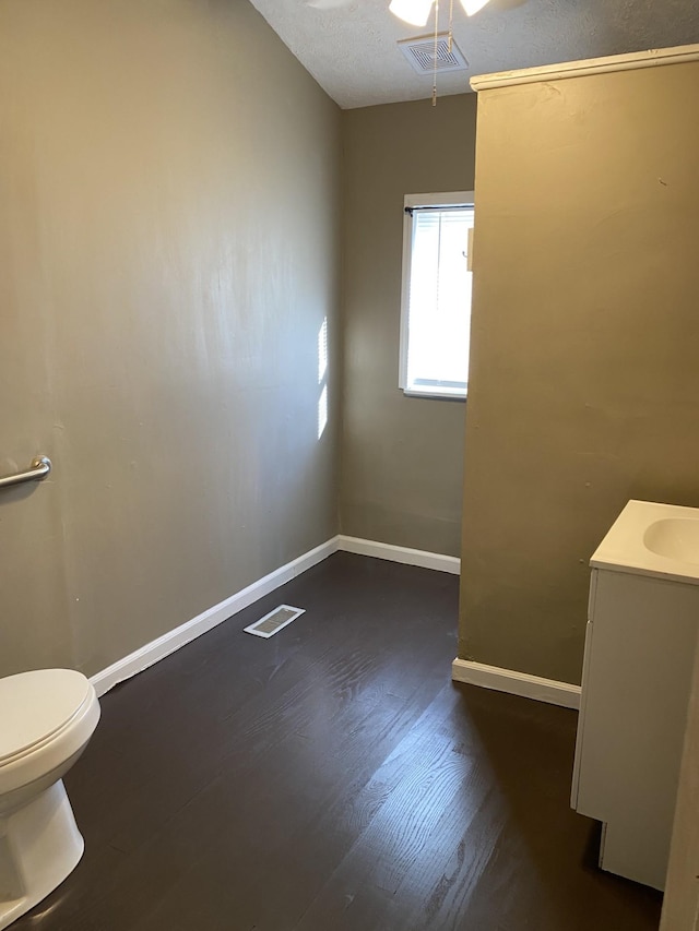 bathroom with ceiling fan, vanity, wood-type flooring, a textured ceiling, and toilet