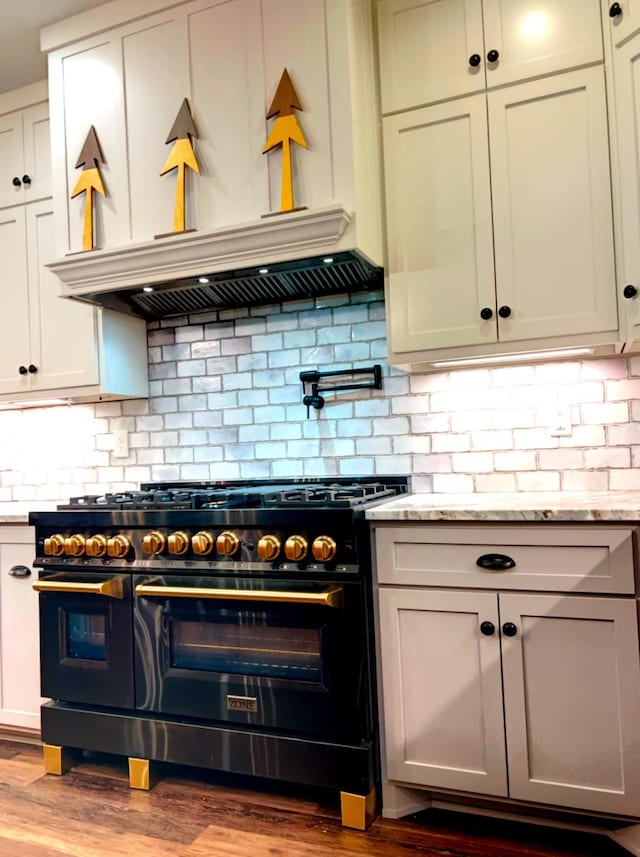 kitchen with decorative backsplash, range with two ovens, custom exhaust hood, light stone counters, and light wood-type flooring