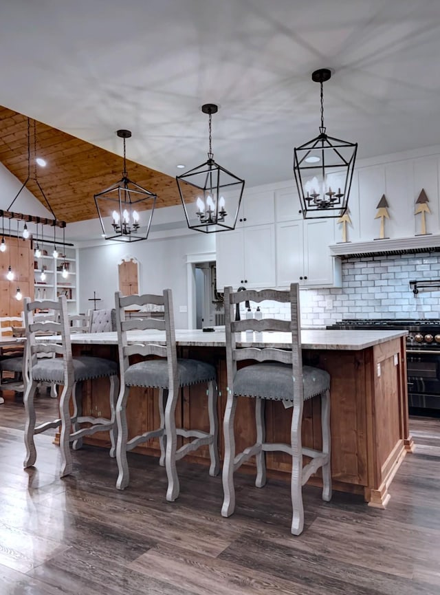 kitchen featuring white cabinetry, decorative light fixtures, light stone countertops, and a center island with sink