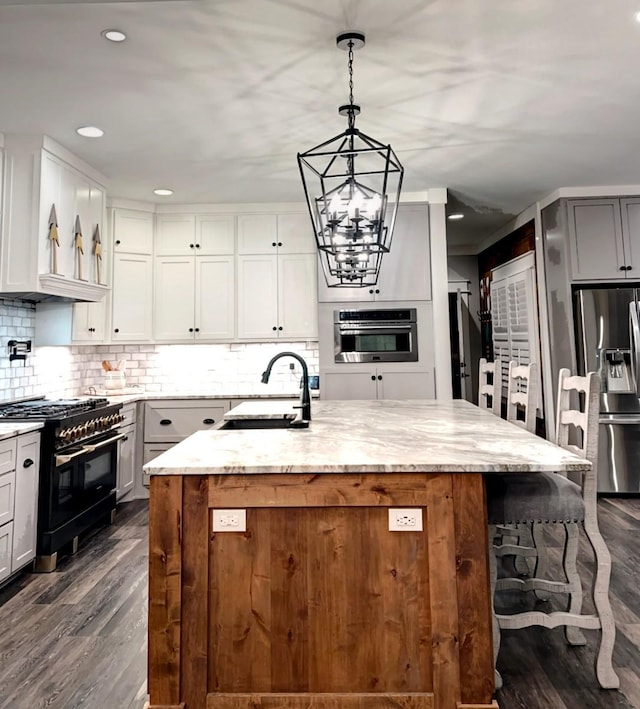 kitchen featuring appliances with stainless steel finishes, an island with sink, sink, decorative backsplash, and light stone countertops