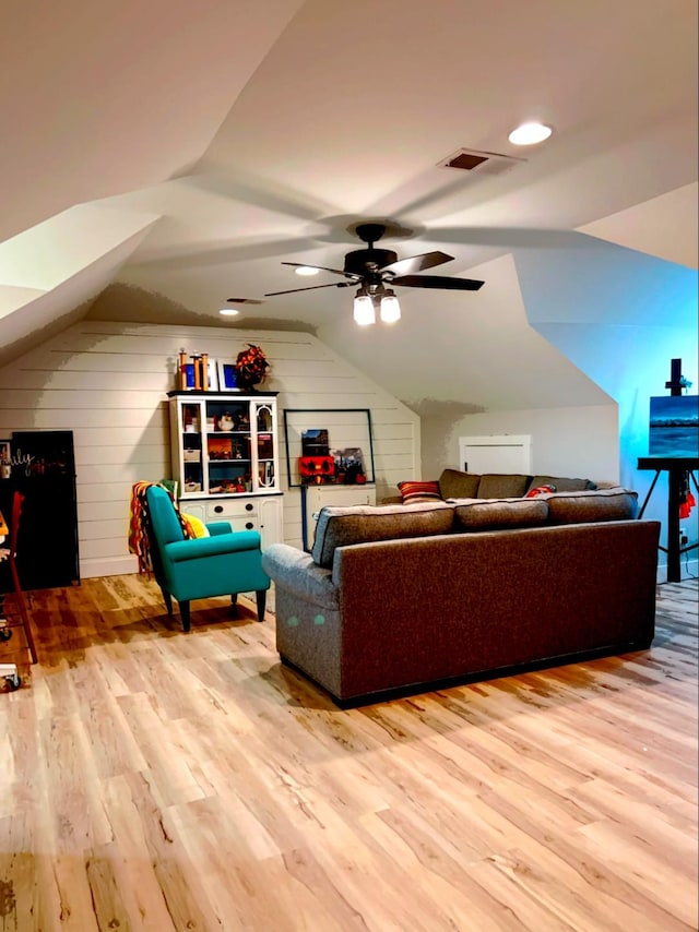 living room with ceiling fan, lofted ceiling, wooden walls, and light wood-type flooring