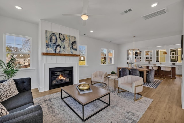 living room with light hardwood / wood-style flooring, a large fireplace, and ceiling fan