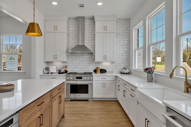 kitchen with appliances with stainless steel finishes, decorative light fixtures, white cabinets, decorative backsplash, and wall chimney exhaust hood