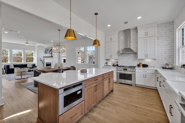 kitchen with a kitchen island, decorative light fixtures, white cabinets, stainless steel appliances, and wall chimney exhaust hood