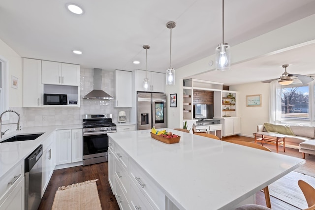 kitchen featuring sink, appliances with stainless steel finishes, a center island, white cabinets, and wall chimney exhaust hood