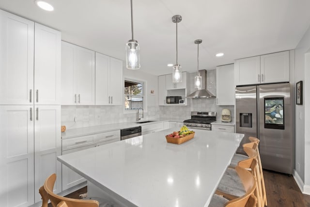 kitchen featuring stainless steel appliances, white cabinetry, a kitchen island, and wall chimney range hood