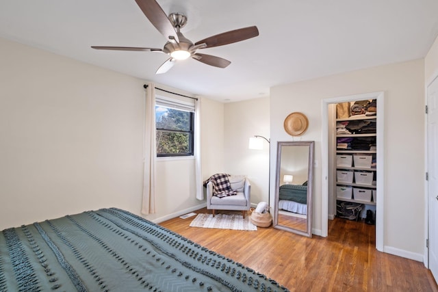 bedroom featuring a spacious closet, wood-type flooring, a closet, and ceiling fan