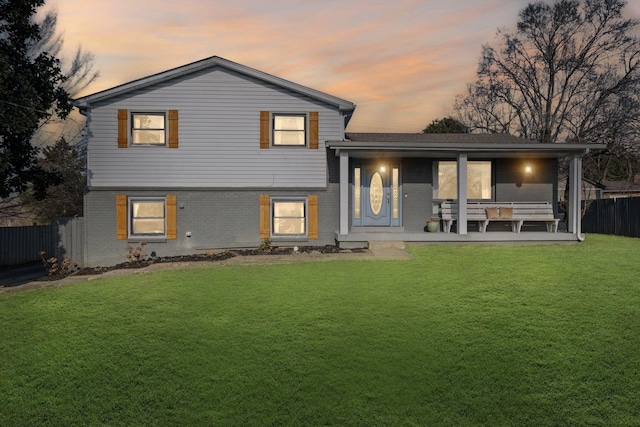 back house at dusk featuring covered porch and a lawn