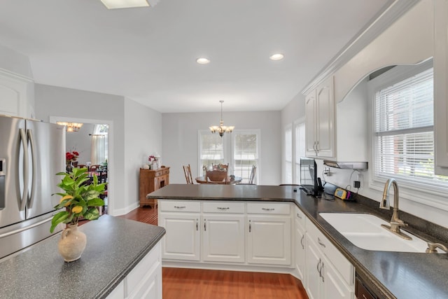 kitchen featuring white cabinetry, stainless steel fridge, kitchen peninsula, and an inviting chandelier