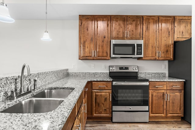 kitchen featuring sink, light stone counters, hardwood / wood-style flooring, pendant lighting, and stainless steel appliances