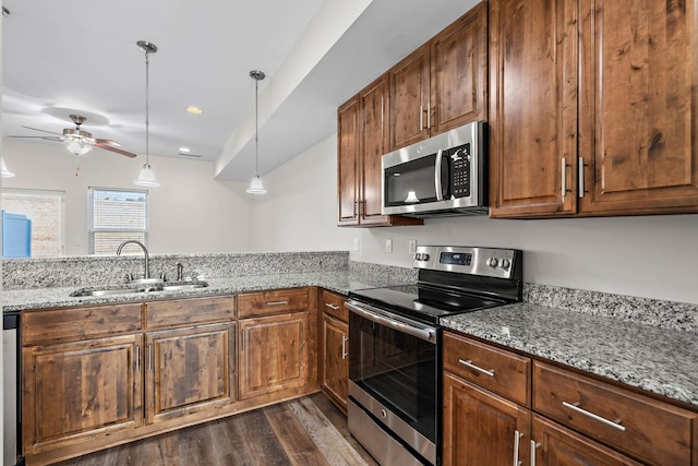 kitchen with light stone counters, stainless steel appliances, sink, and pendant lighting