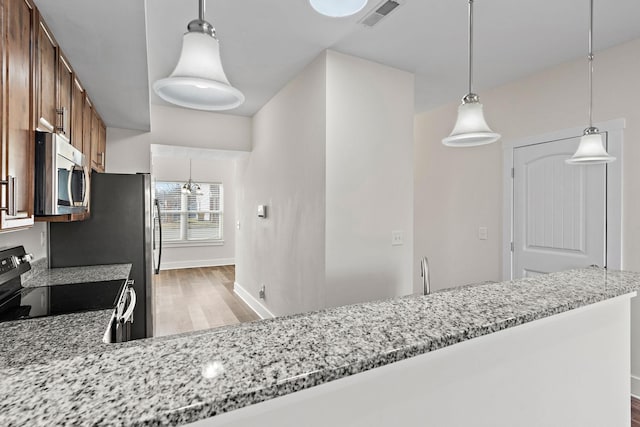 kitchen with light stone counters, stainless steel appliances, light hardwood / wood-style floors, and hanging light fixtures