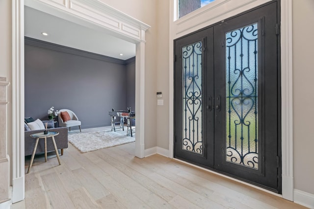 foyer entrance with ornamental molding, french doors, and light wood-type flooring