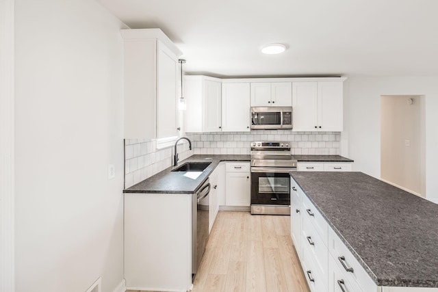 kitchen featuring sink, light wood-type flooring, appliances with stainless steel finishes, white cabinets, and backsplash