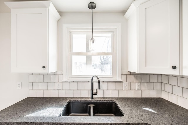 kitchen with sink, white cabinets, pendant lighting, dark stone counters, and backsplash