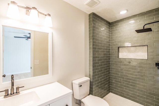 bathroom featuring vanity, tiled shower, ceiling fan, toilet, and a textured ceiling