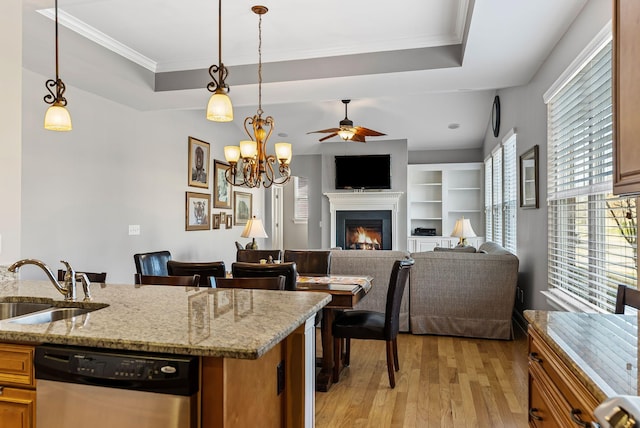 kitchen featuring stainless steel dishwasher, a tray ceiling, light stone countertops, and sink