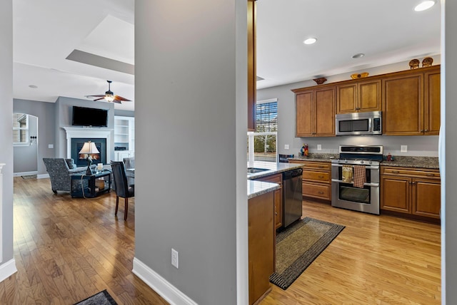 kitchen with light stone counters, light wood-type flooring, ceiling fan, and appliances with stainless steel finishes