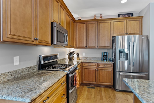 kitchen featuring light stone counters, stainless steel appliances, and light wood-type flooring