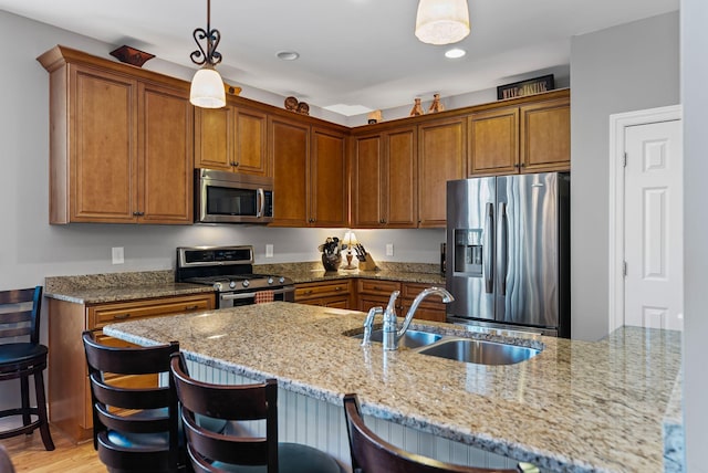 kitchen featuring sink, a breakfast bar area, hanging light fixtures, stainless steel appliances, and light stone counters