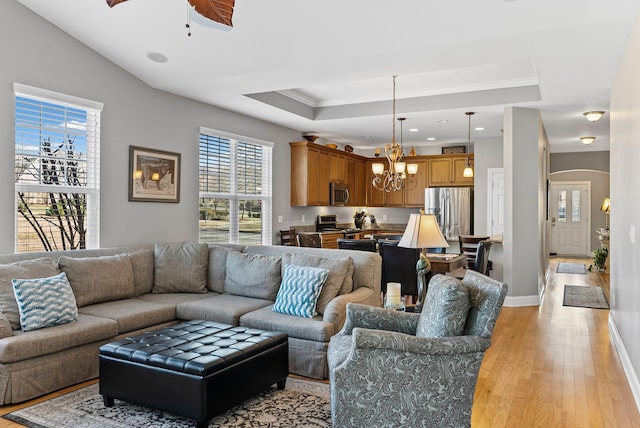 living room with a raised ceiling, crown molding, ceiling fan with notable chandelier, and light hardwood / wood-style floors