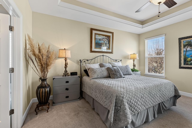 carpeted bedroom with ceiling fan and a raised ceiling